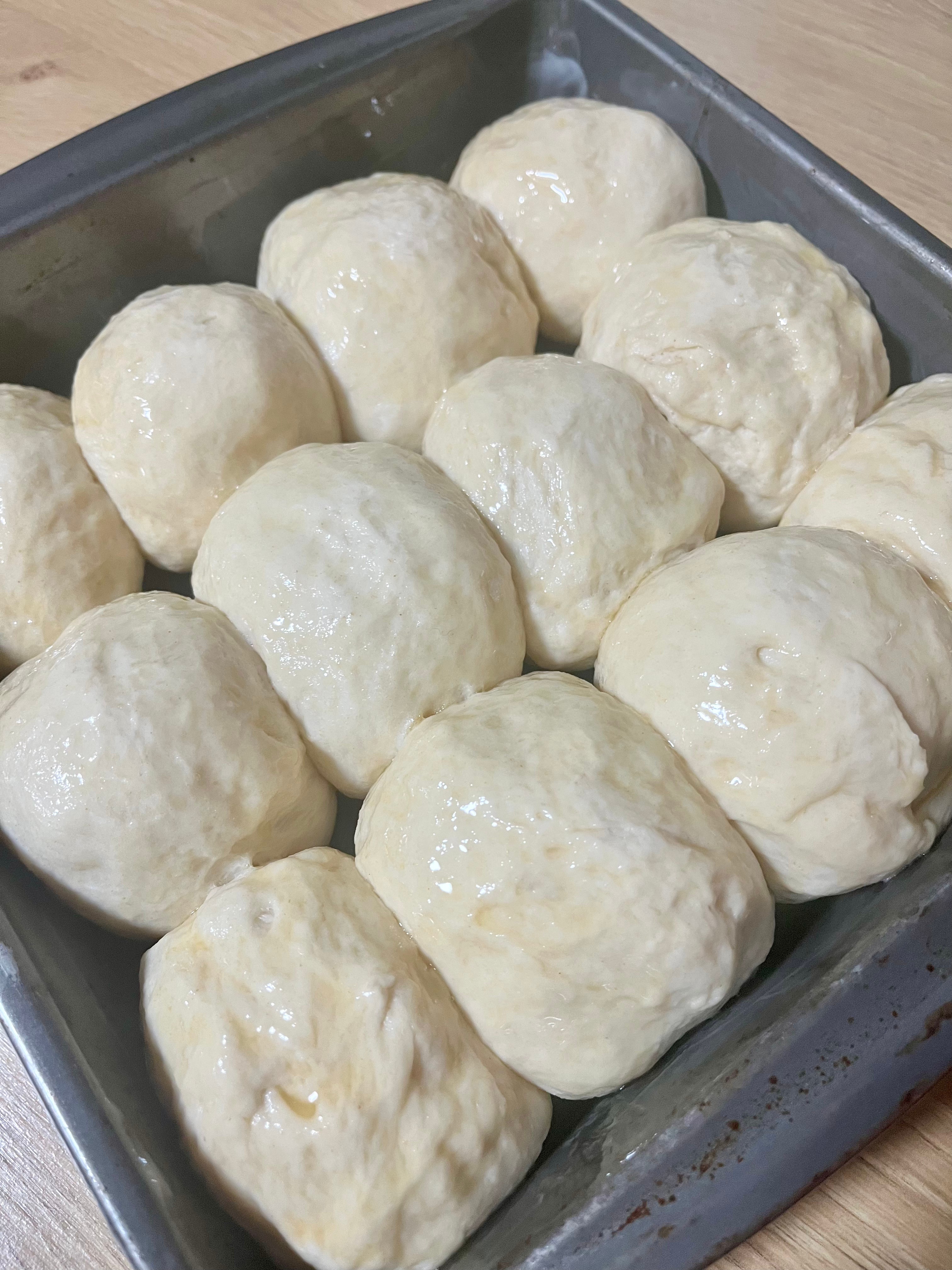 Twelve unbaked dough rolls arranged in a baking pan ready for the oven.